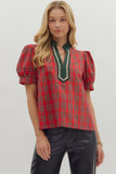 Woman wearing a red plaid blouse with green accents on a plain background