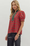 Woman wearing a red plaid blouse with green trim on a plain background