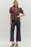 Woman wearing a plaid top with red trim and black pants on a white background