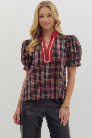 Woman wearing a plaid blouse with red accents and black pants on a white background