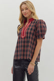 Woman wearing a plaid top with red accents on a plain background