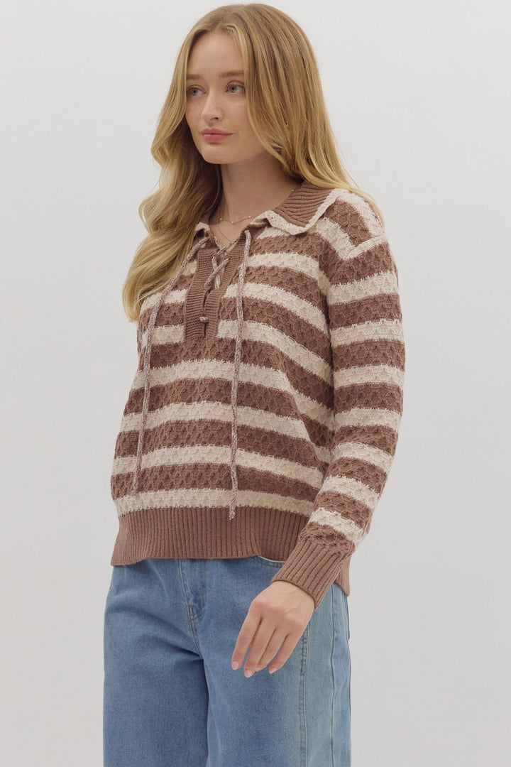 Woman wearing a brown and white striped sweater with blue jeans on a plain background