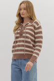 Woman wearing a brown and white striped sweater with blue jeans on a plain background