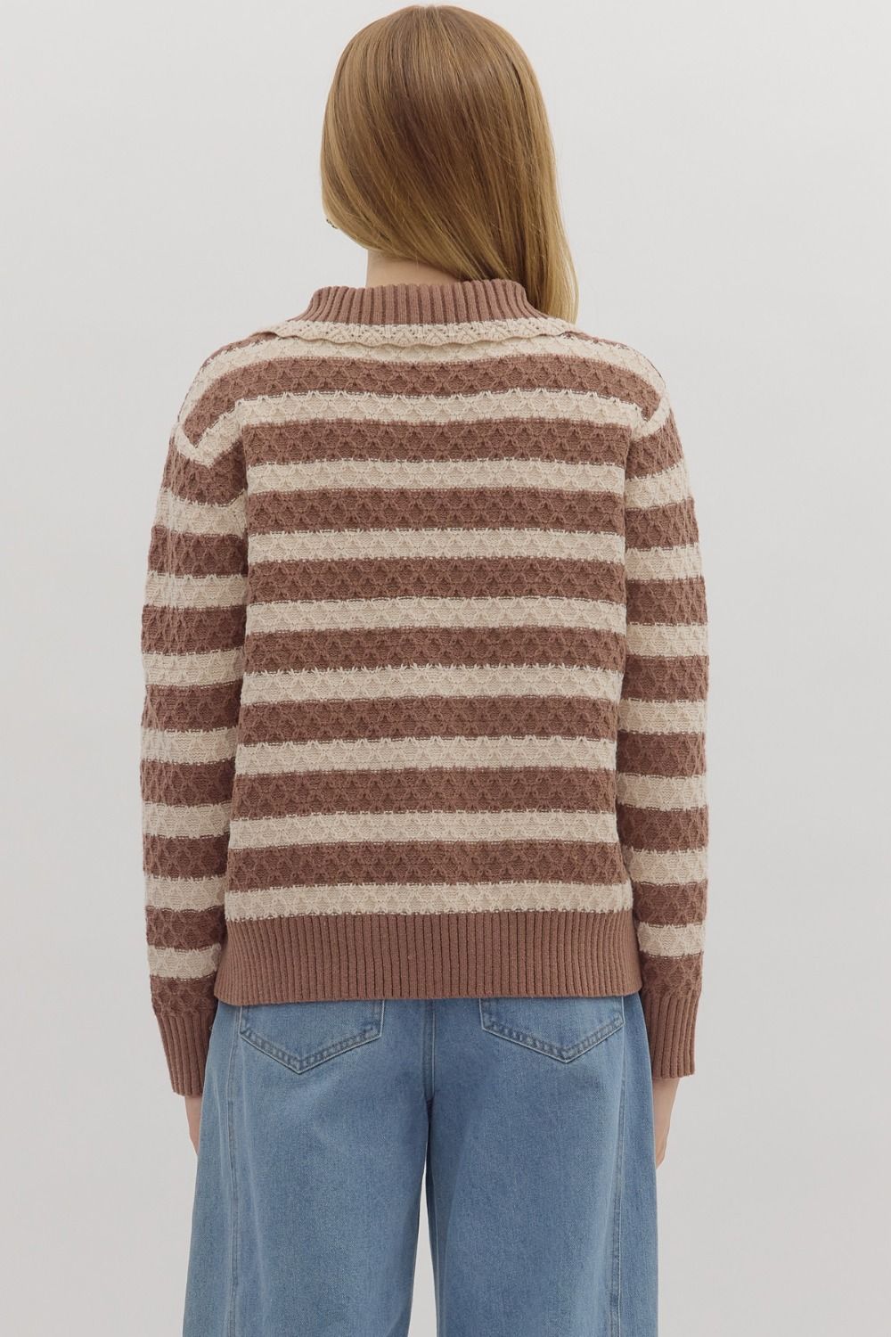 Person wearing a brown and beige striped sweater with blue jeans on a white background