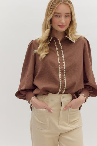Woman wearing a brown blouse with white trim and beige pants on a white background
