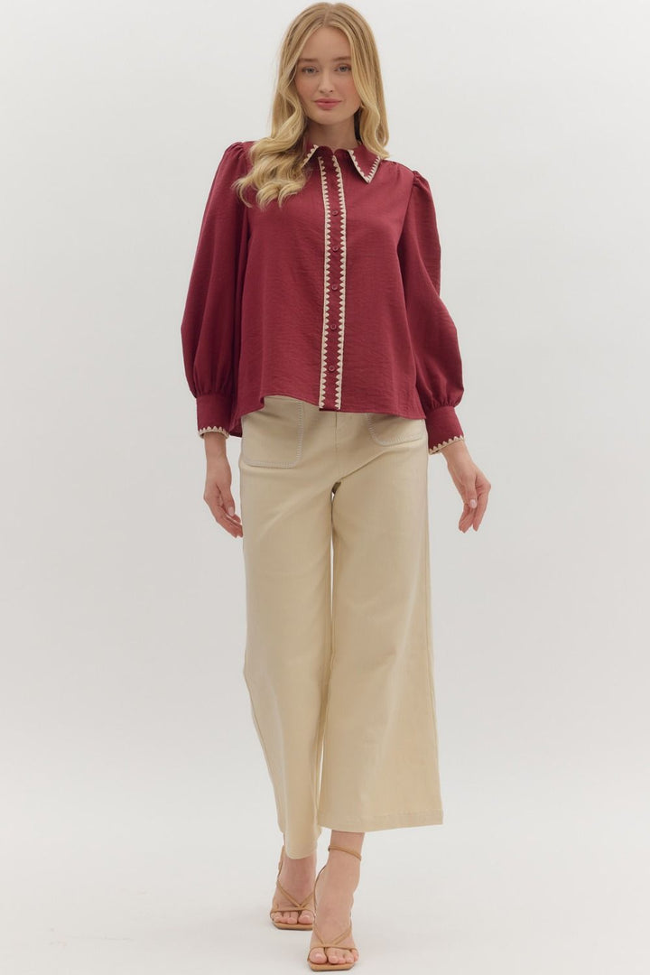 Woman wearing a burgundy blouse with white trim and beige pants on a white background