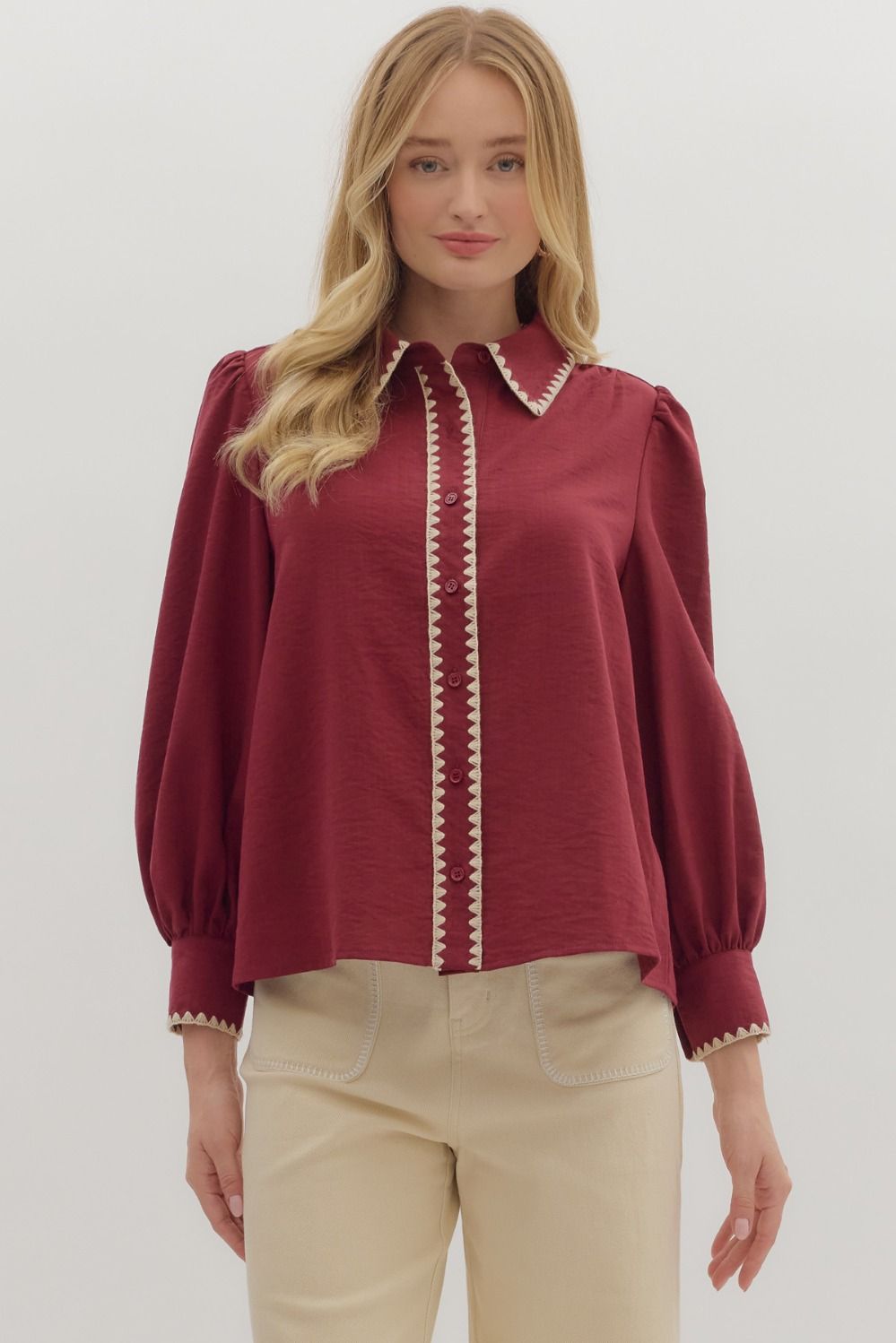 Woman wearing a burgundy blouse with white trim on a plain background