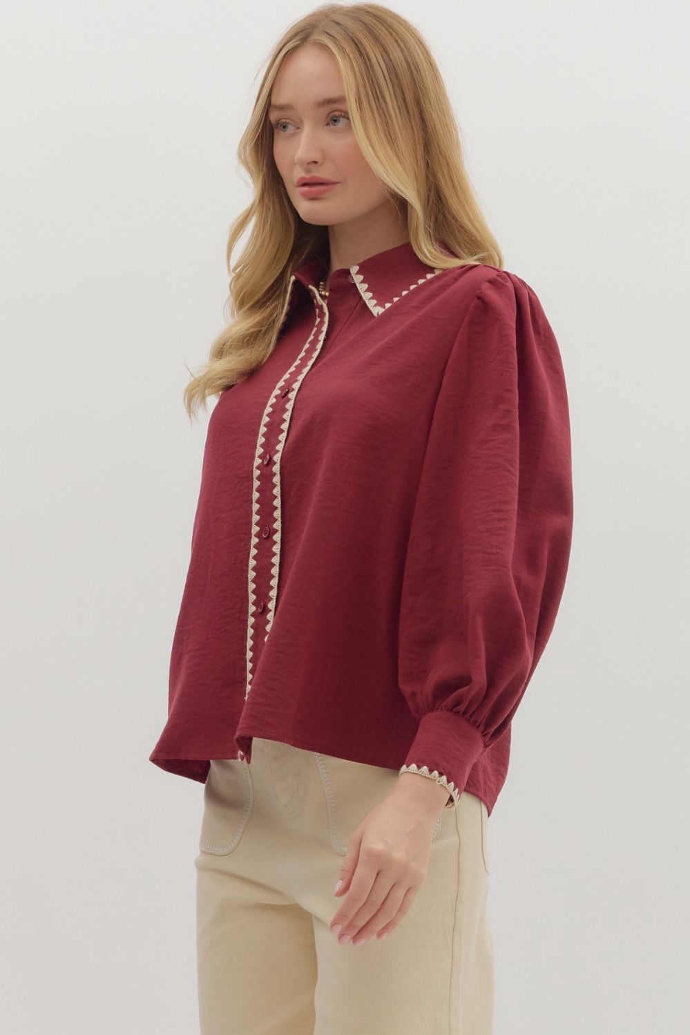 Woman wearing a burgundy blouse with white trim on a plain background