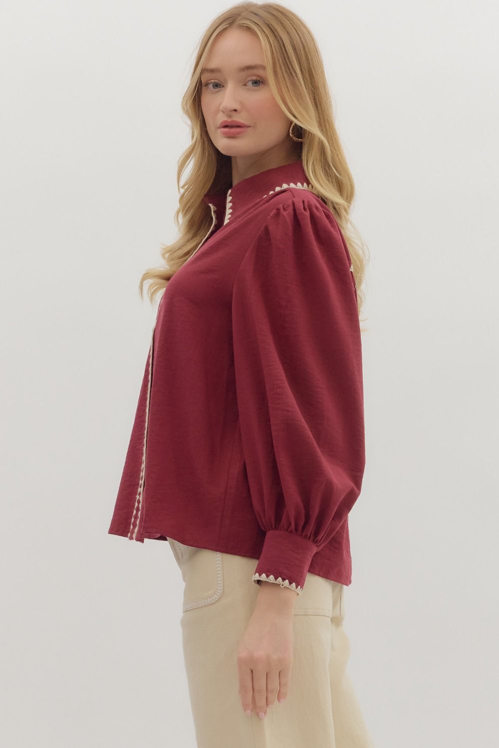 Woman wearing a burgundy blouse with white trim on a plain background