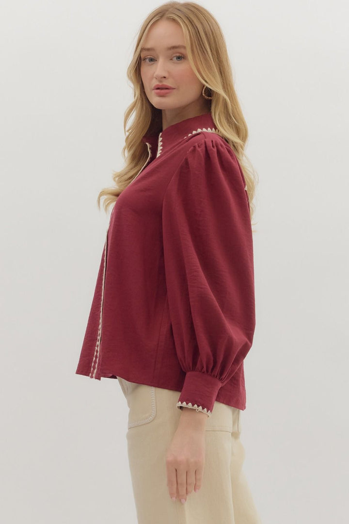 Woman wearing a burgundy blouse with white trim on a plain background