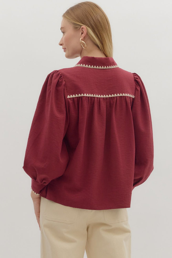 Woman wearing a burgundy blouse with pearl embellishments on a plain background