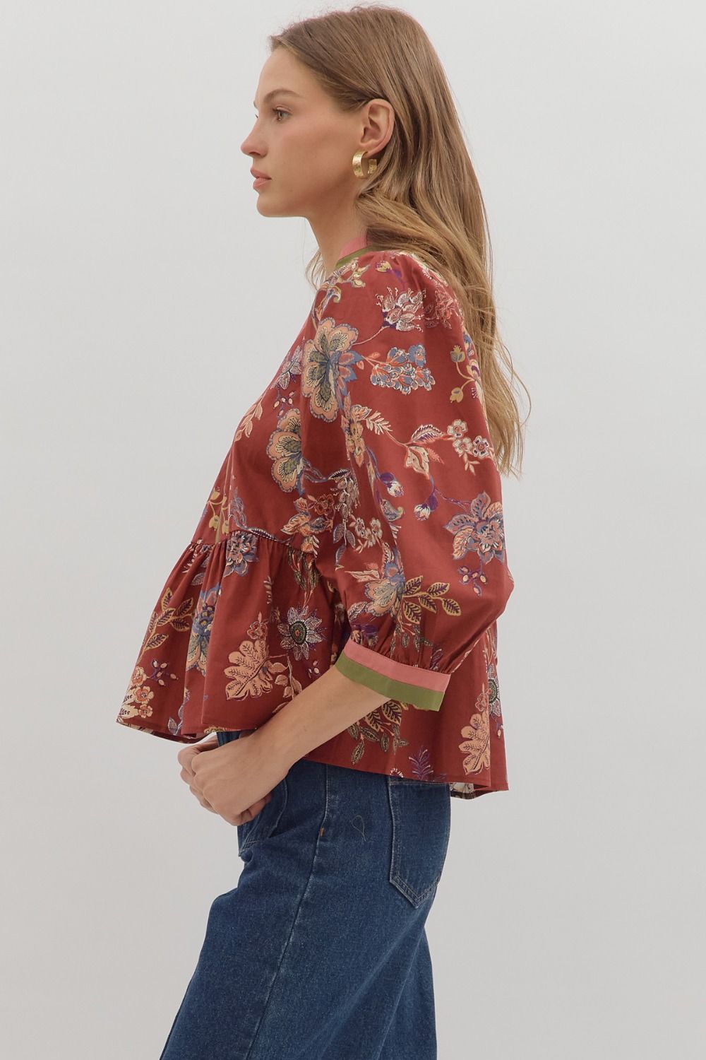 Woman wearing a red floral blouse and blue jeans on a plain background