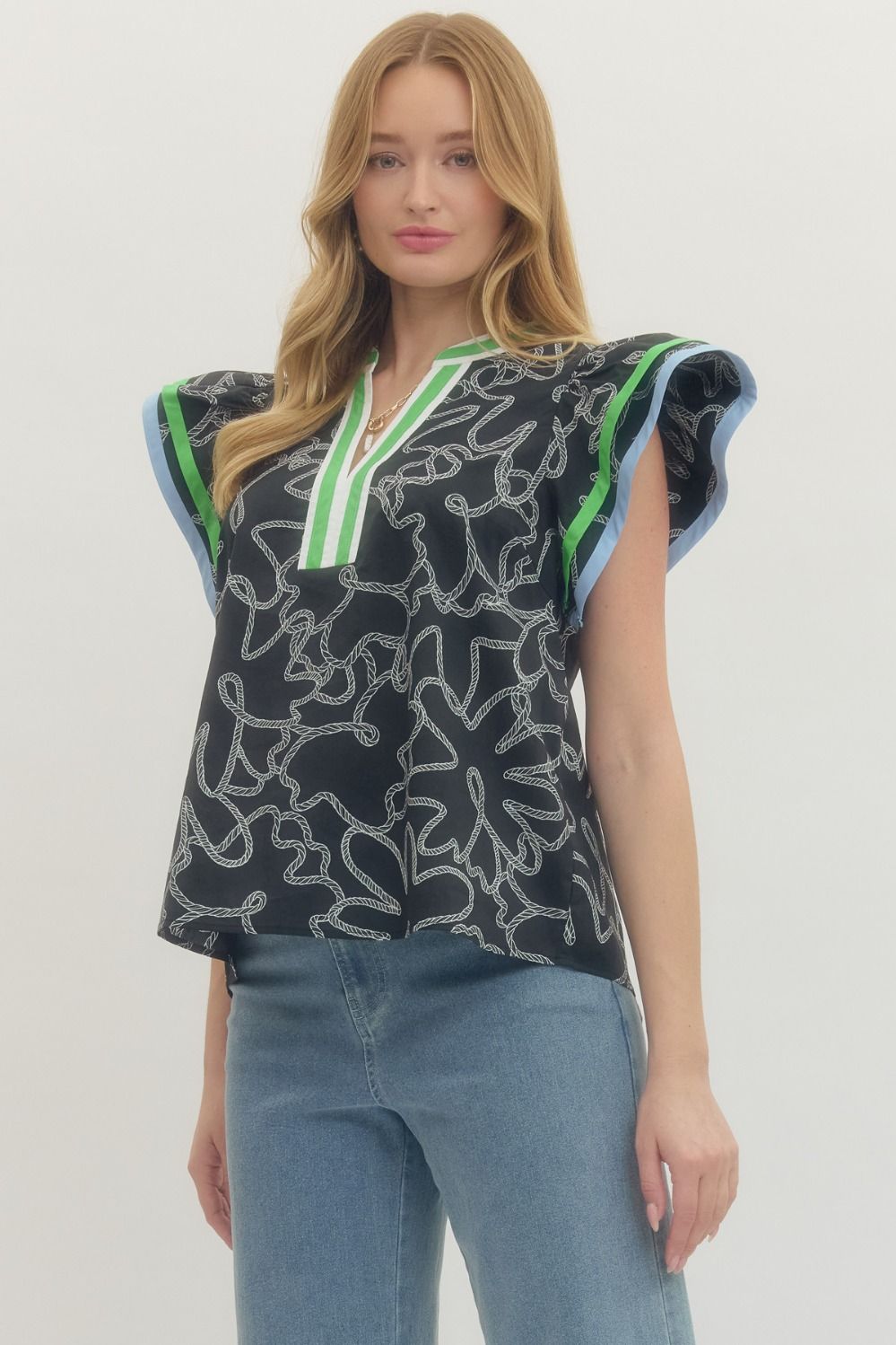 Woman wearing a black patterned top with green accents and blue jeans on a white background