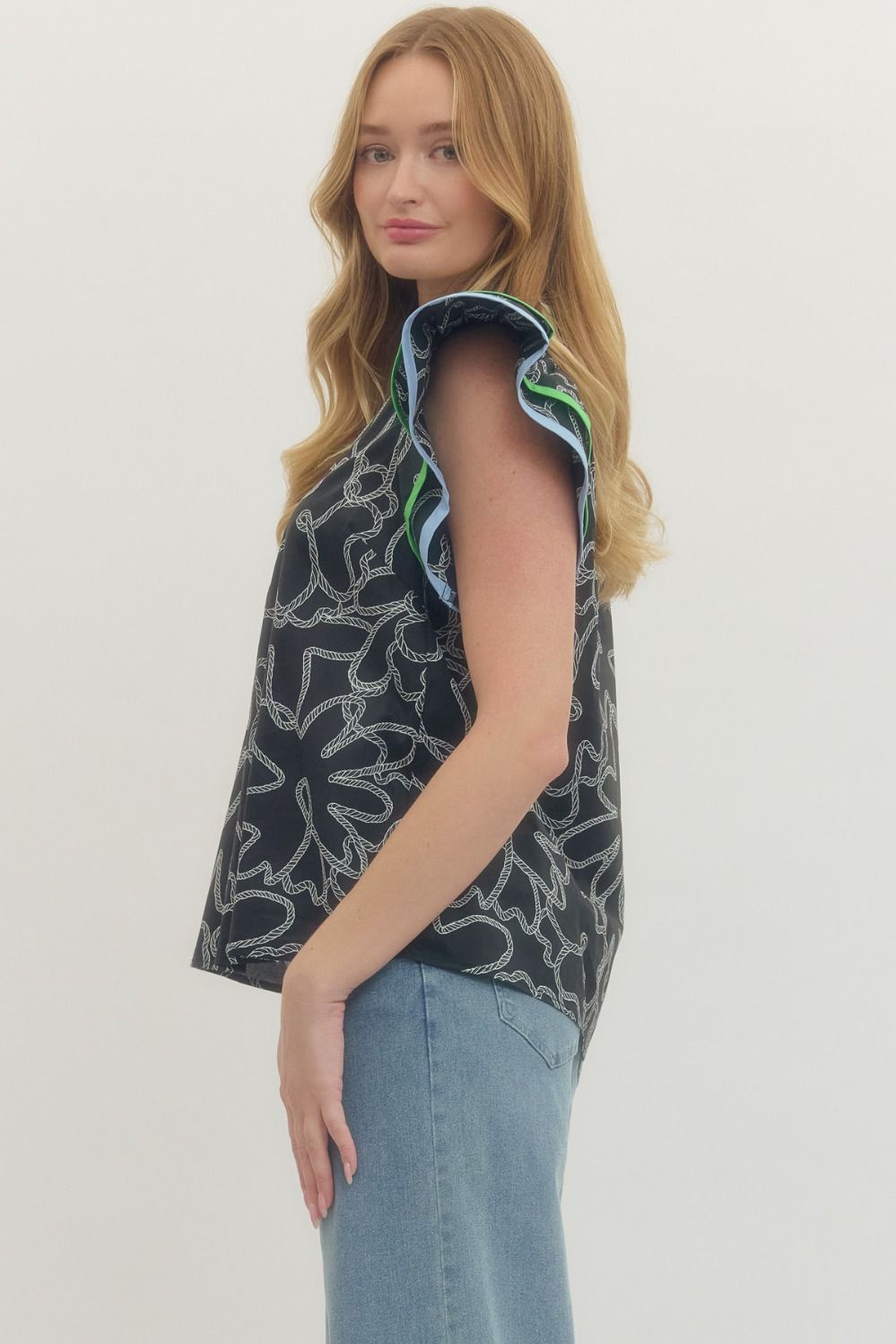 Woman wearing a sleeveless patterned top and light blue jeans on a white background