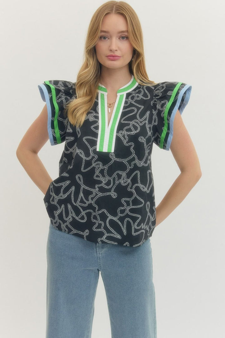 Woman wearing a black patterned top with green accents and blue jeans on a white background