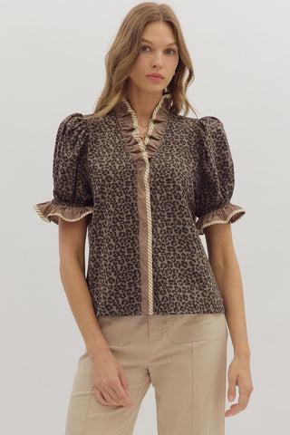 Woman wearing a leopard print blouse with ruffled details on a plain background