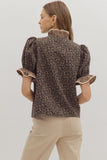 Woman wearing a leopard print blouse with ruffled sleeves on a plain background