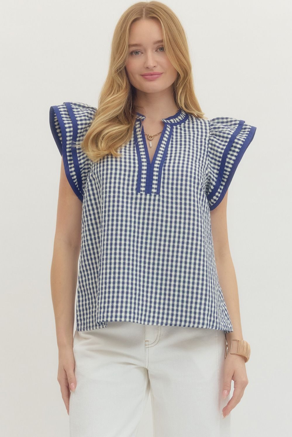 Woman wearing a blue and white checkered top with ruffled sleeves on a white background