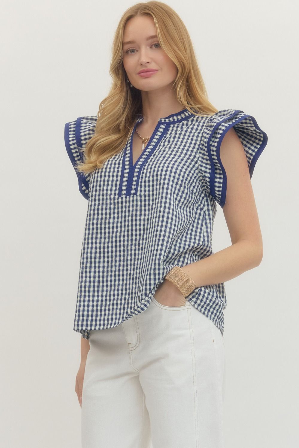 Woman wearing a blue and white checkered top with ruffled sleeves on a plain background