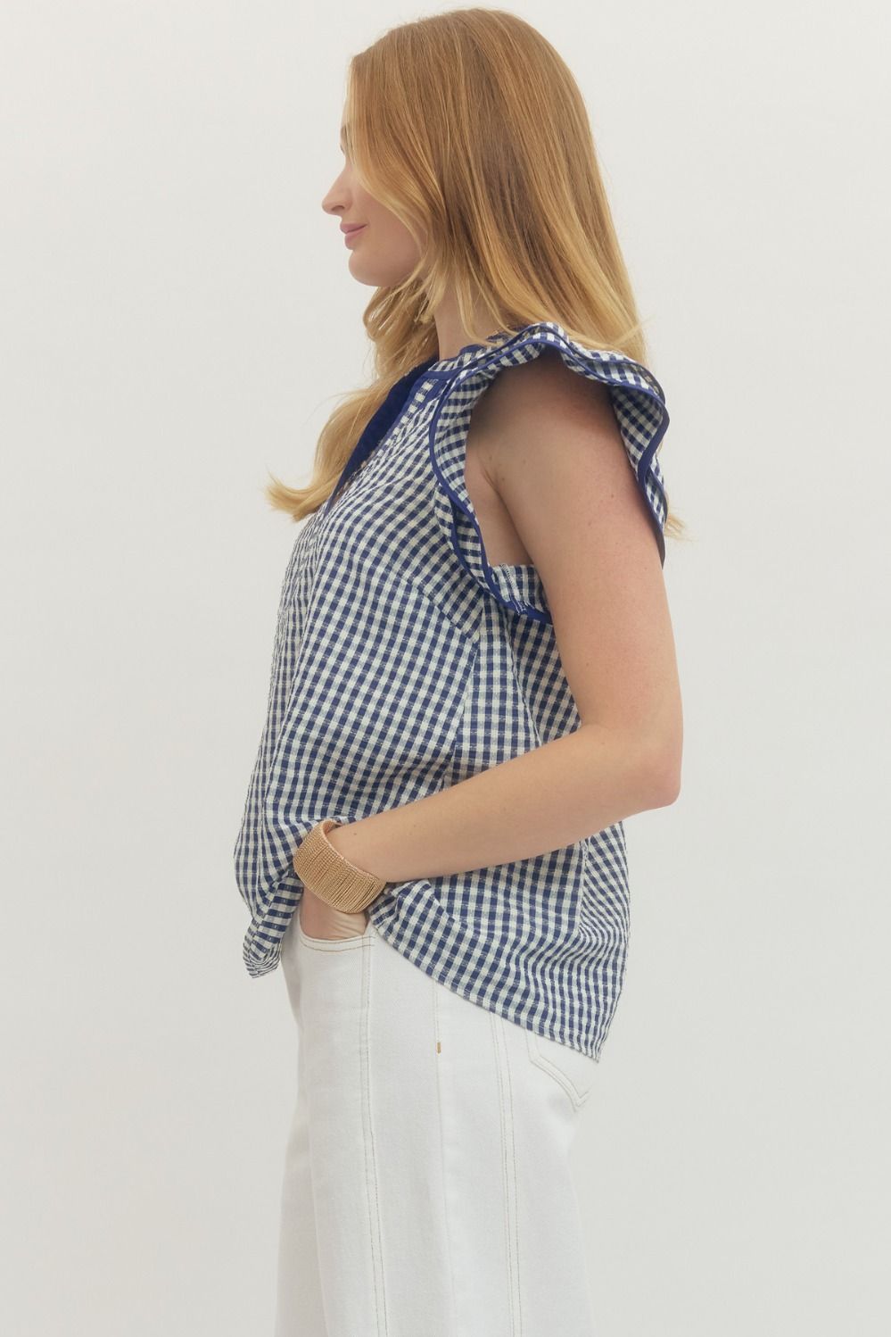 Woman wearing a blue and white checkered top with ruffled sleeves on a plain background