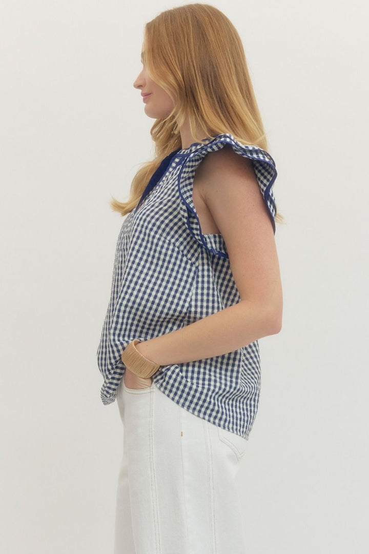 Woman wearing a blue and white checkered top with ruffled sleeves on a plain background