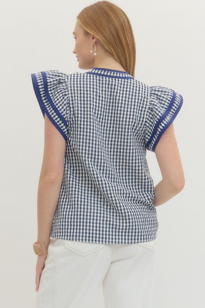 Woman wearing a blue and white checkered top with ruffled sleeves on a white background
