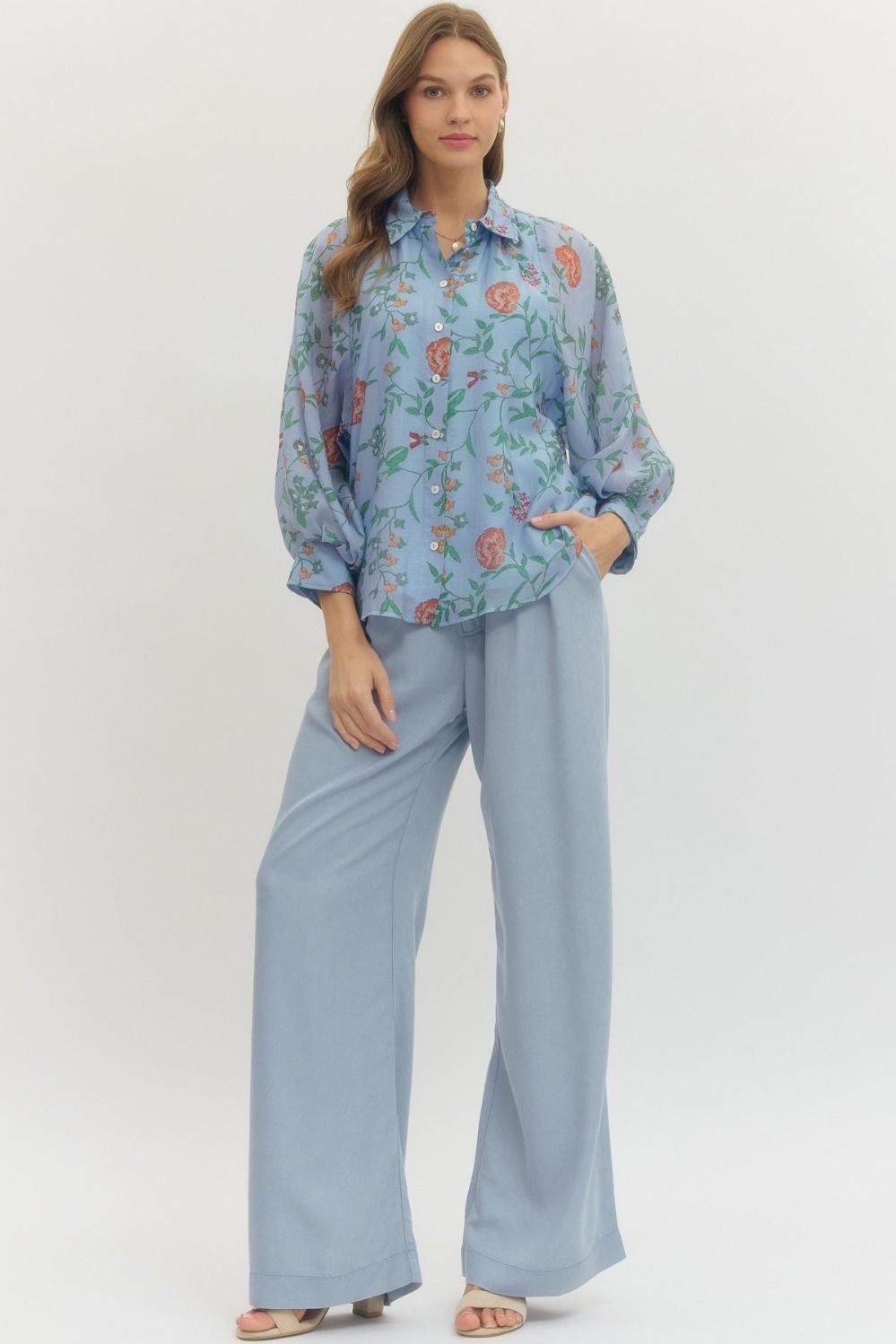 Woman wearing a floral blouse and light blue pants on a white background