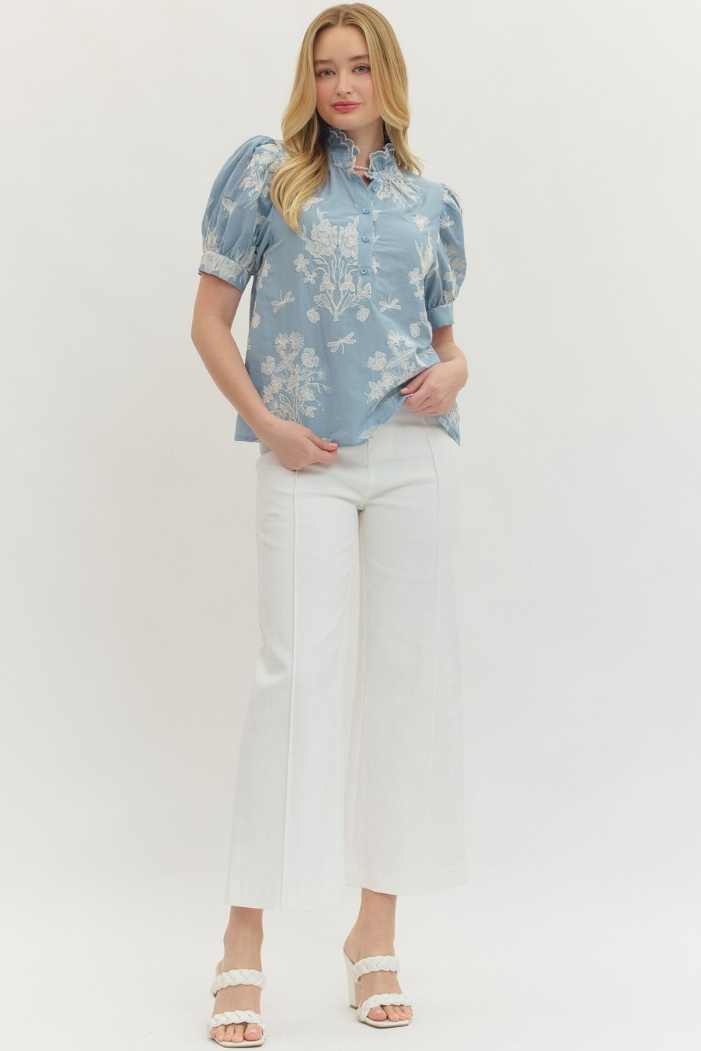 Woman wearing a blue floral blouse and white pants on a white background
