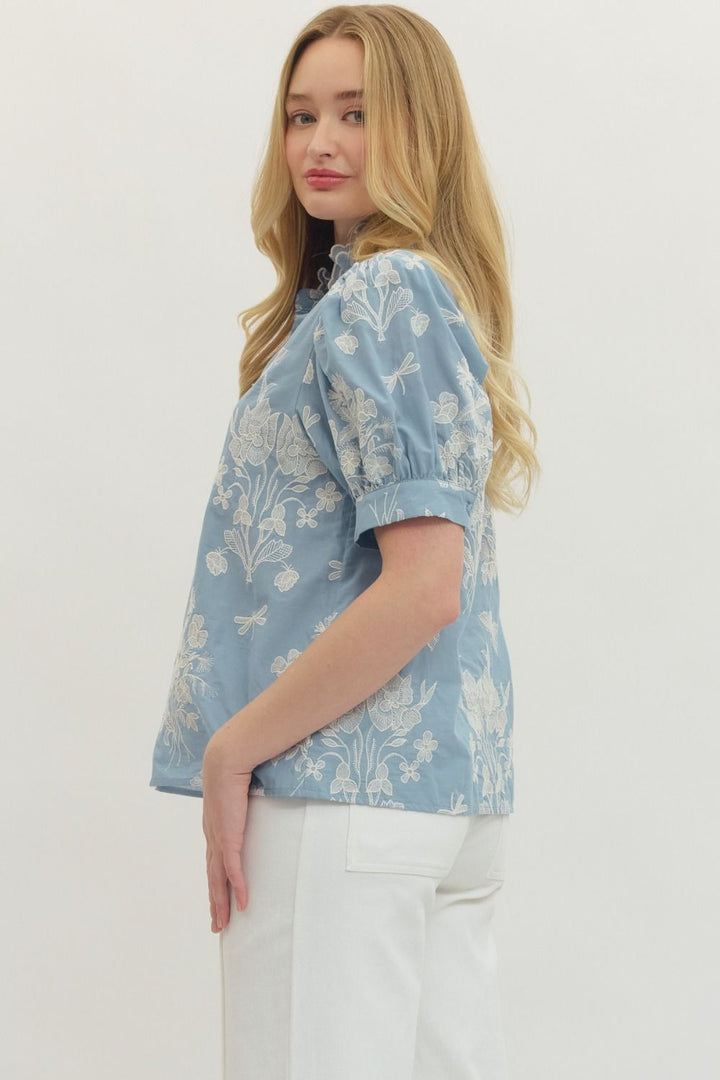 Light blue blouse with white floral embroidery on a plain background