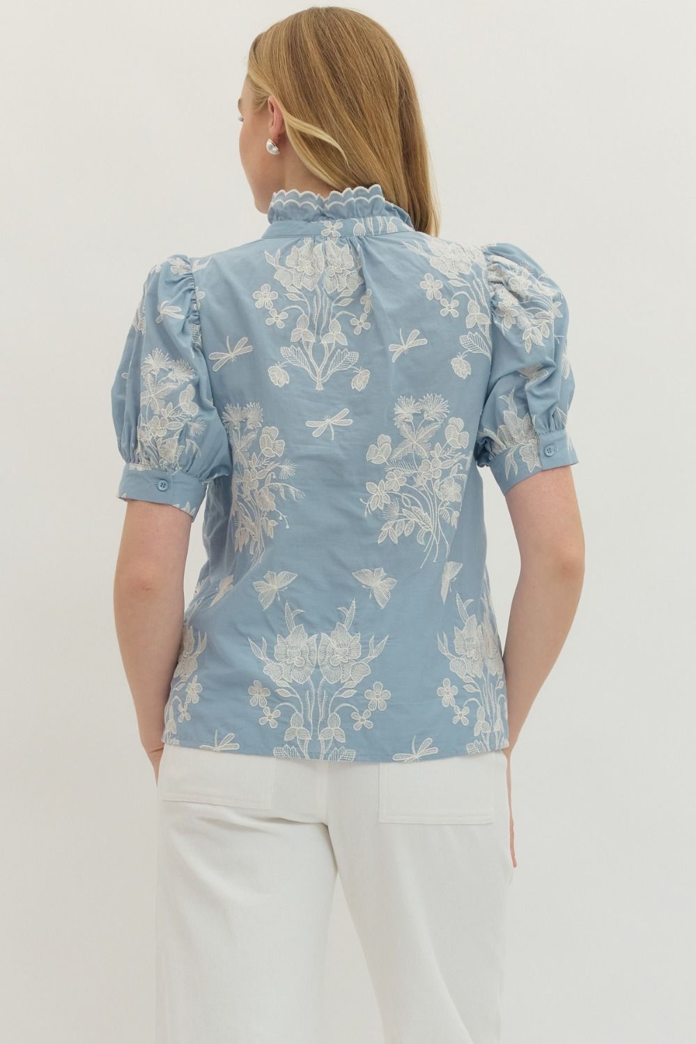 Woman wearing a blue floral blouse with white pants on a white background