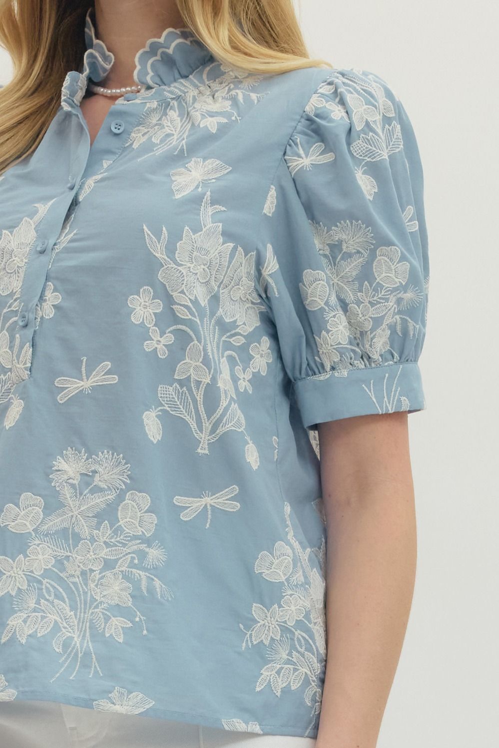 Light blue floral and dragonfly patterned blouse on a plain background