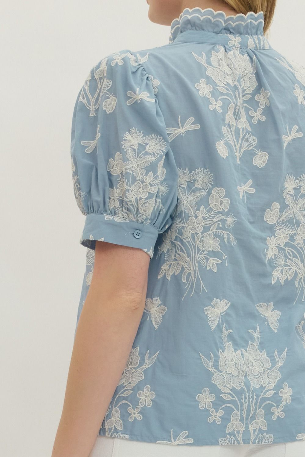 Light blue blouse with white floral embroidery on a plain background