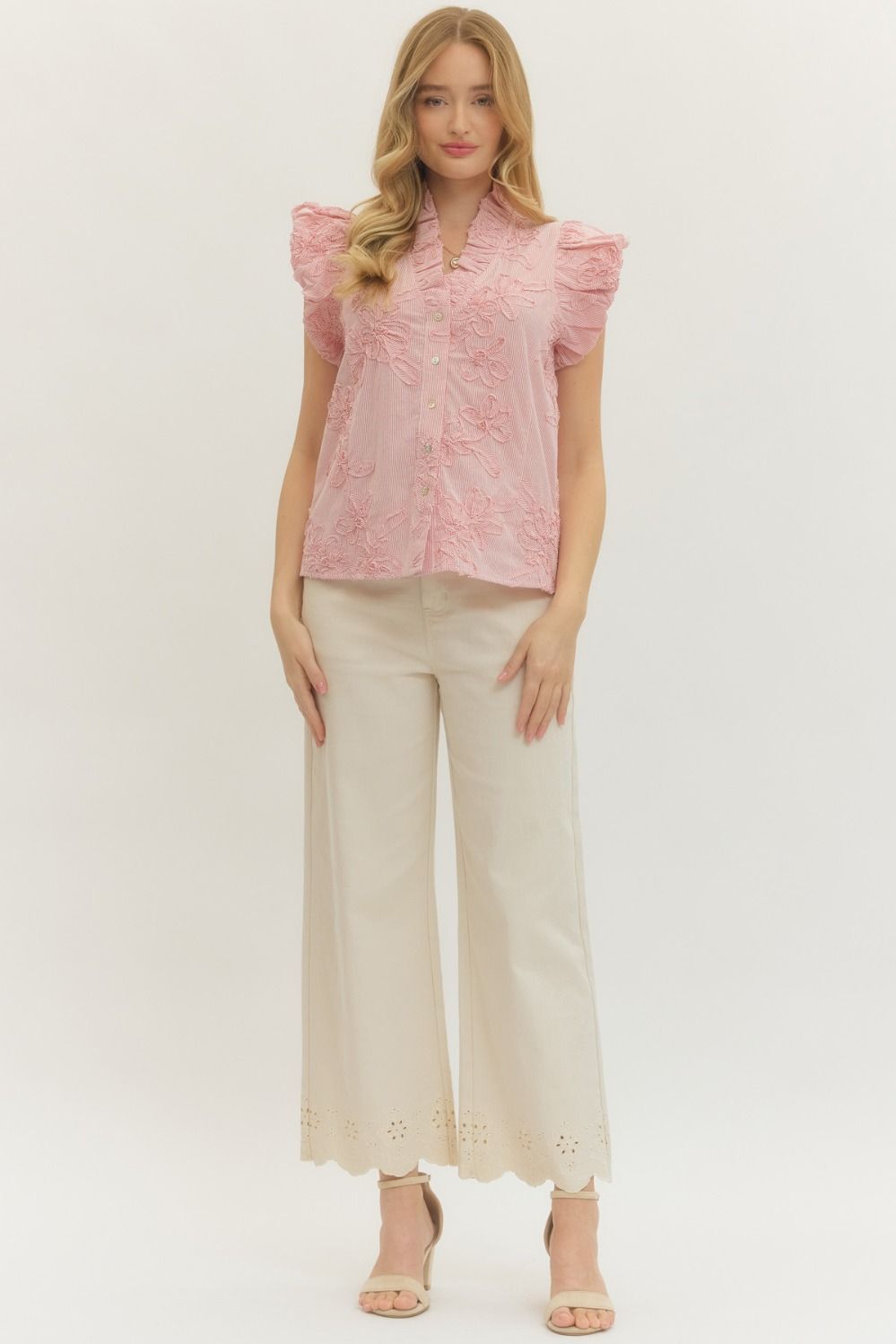 Woman wearing a pink blouse with ruffled sleeves and beige pants on a white background