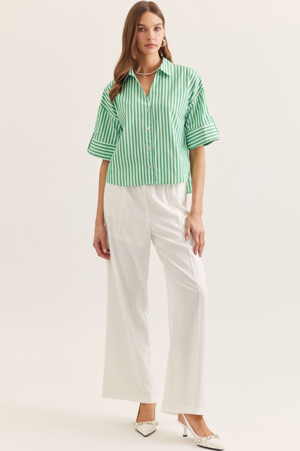 Woman wearing a green and white striped shirt with white pants on a light background
