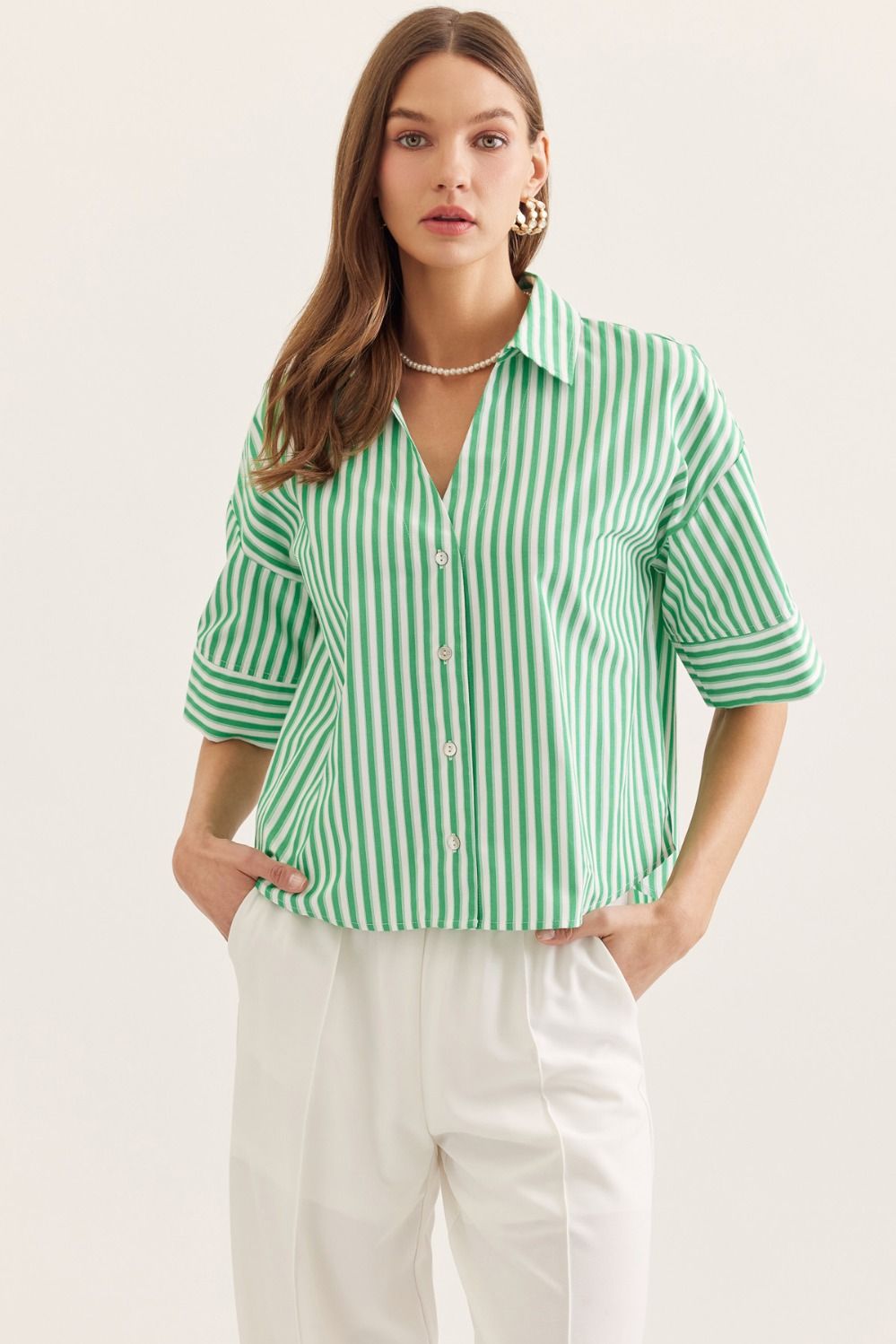 Woman wearing a green and white striped shirt with white pants on a plain background