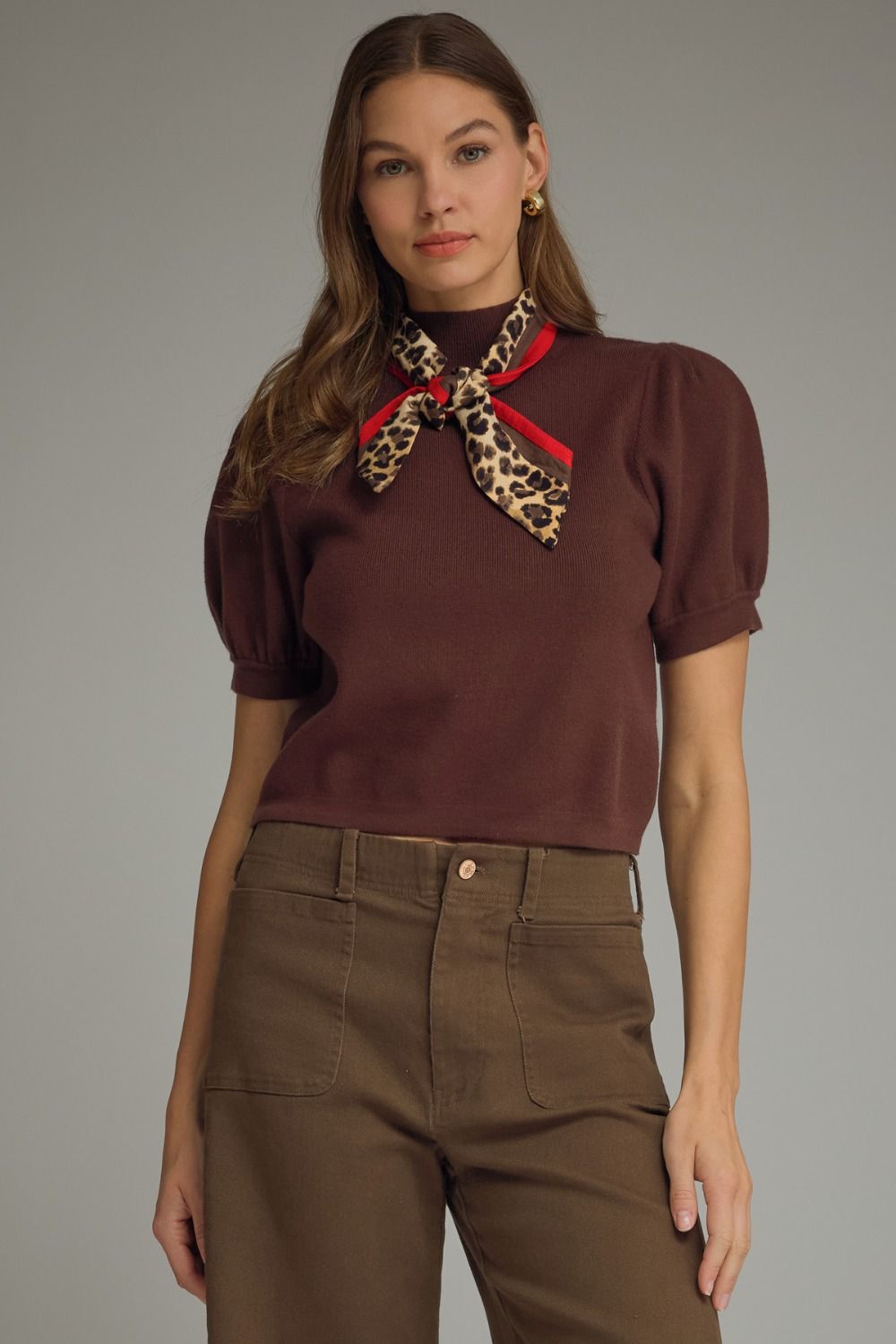 Woman wearing a brown blouse with a leopard print scarf against a gray background