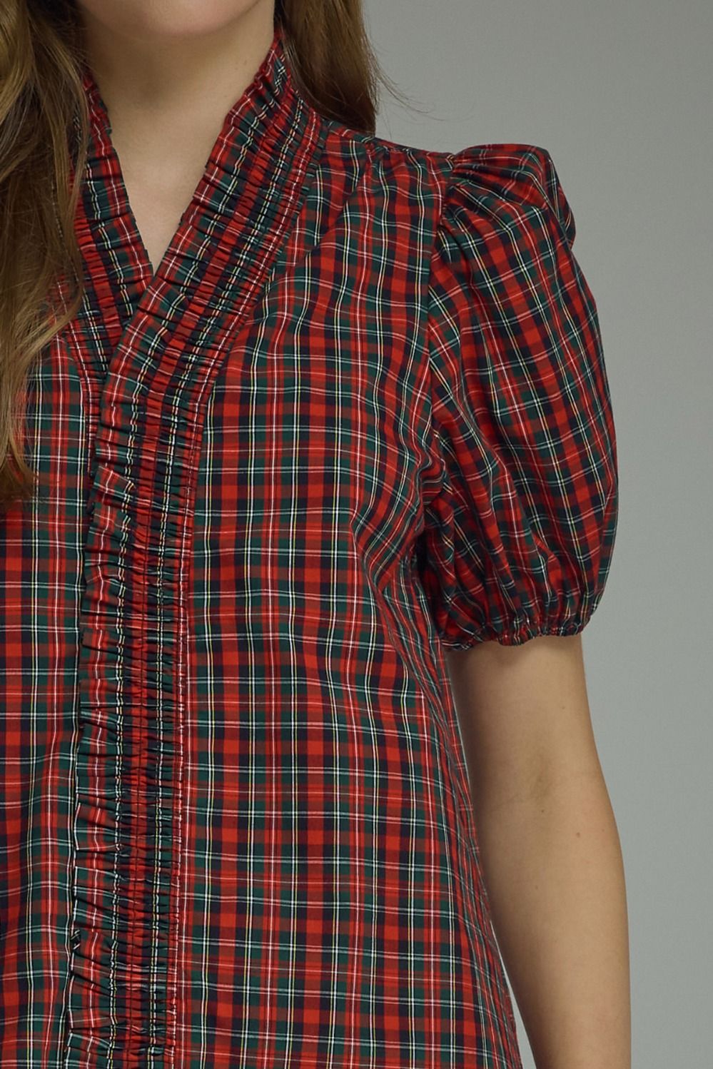 A close-up of a model wearing a red and black plaid short-sleeve blouse with puffed sleeves and a gathered front.