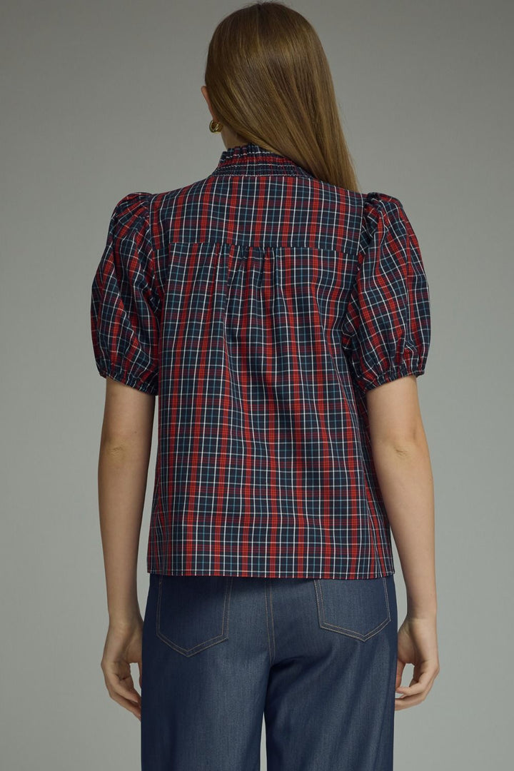 A woman viewed from the back wearing a short-sleeve plaid blouse with puff sleeves and dark blue jeans, against a plain gray studio background.