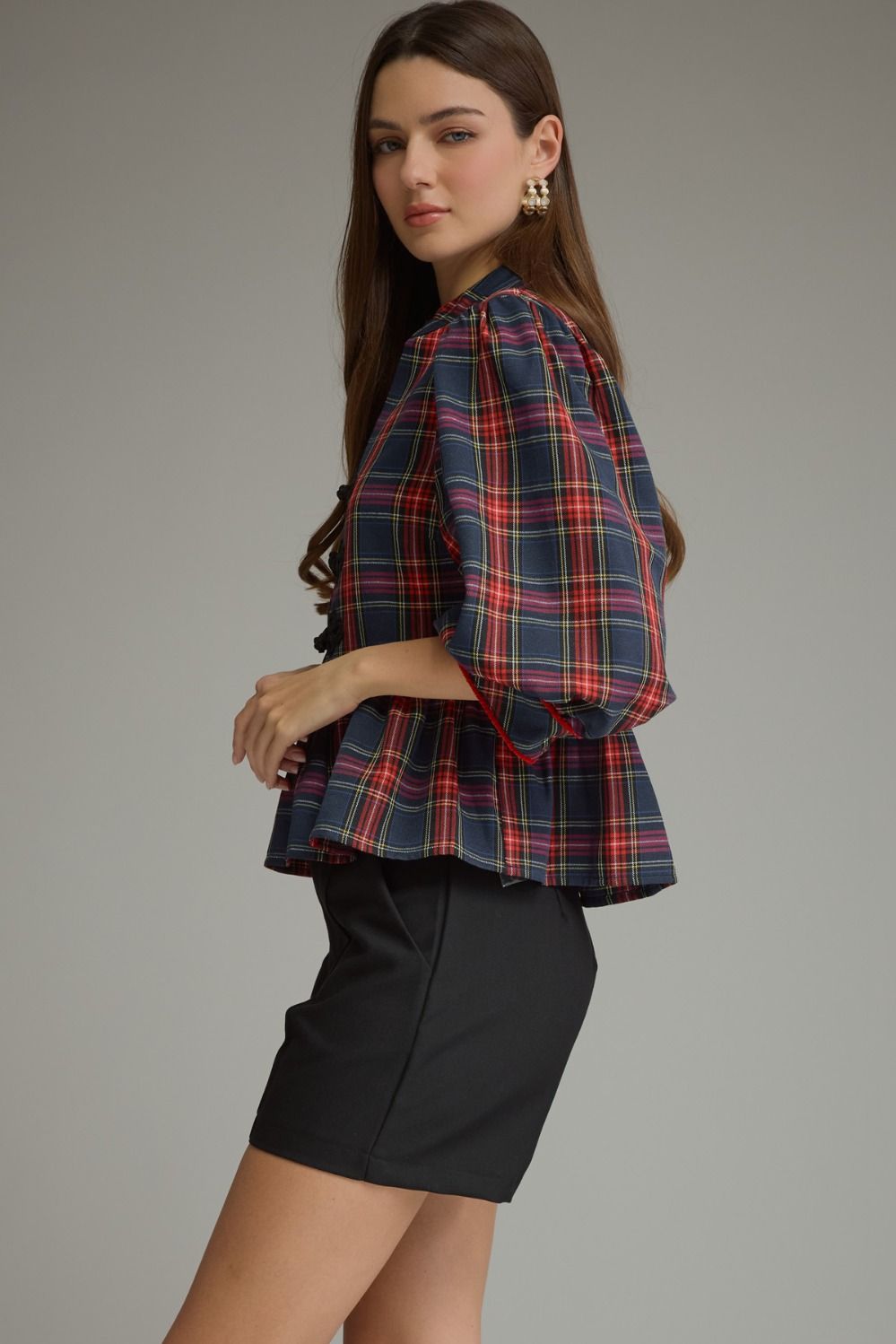 A woman modeling a navy blue plaid blouse with red and yellow stripes, paired with a black mini skirt, against a solid gray studio background.