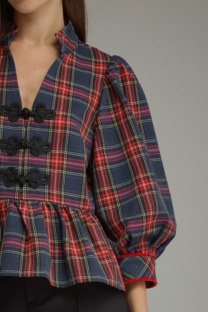 A close-up of a woman wearing a navy blue plaid blouse with red, yellow, and white stripes, featuring black decorative front buttons and a peplum hem.