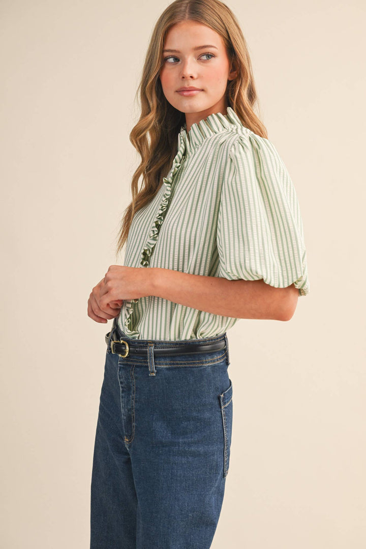 Woman wearing a green and white striped blouse with blue jeans on a beige background