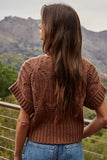 Woman wearing a brown knitted sweater with a mountainous landscape in the background