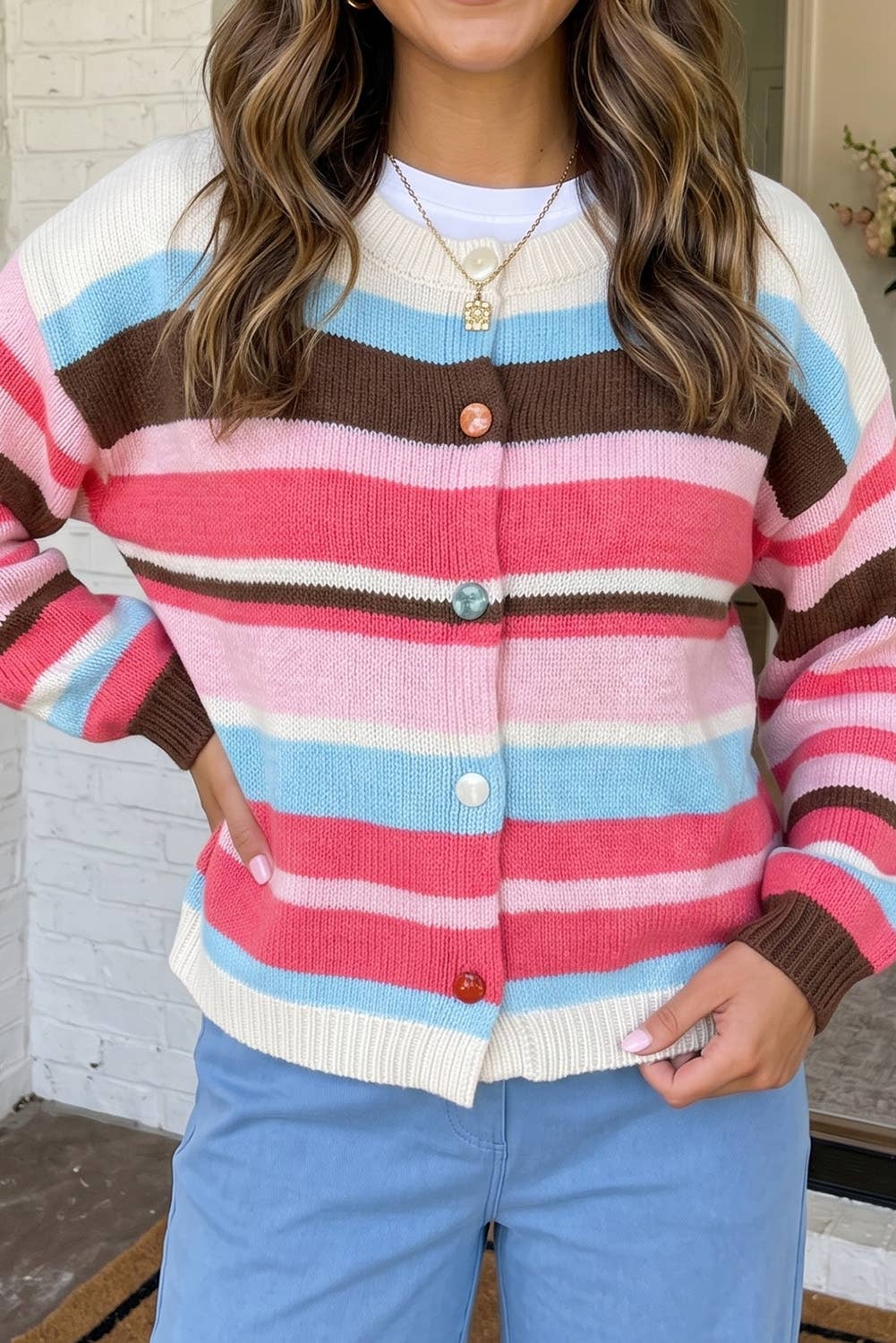 A woman wearing a colorful striped cardigan sweater with pink, light blue, brown, and cream horizontal stripes, paired with light blue pants.