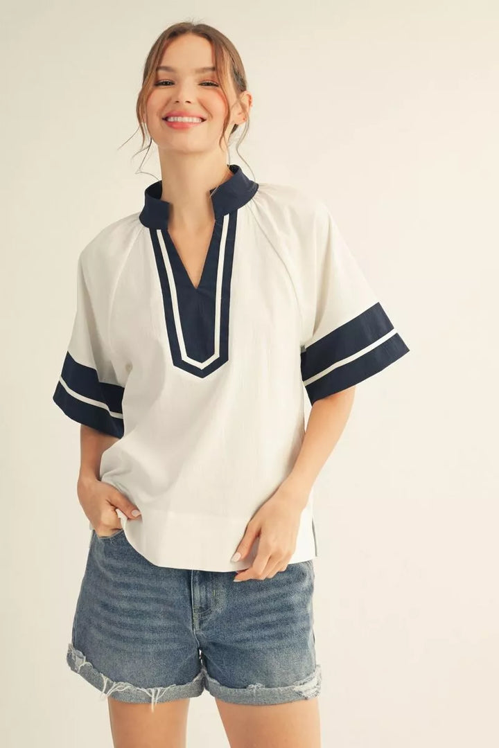 Woman wearing a white blouse with navy accents and denim shorts on a beige background