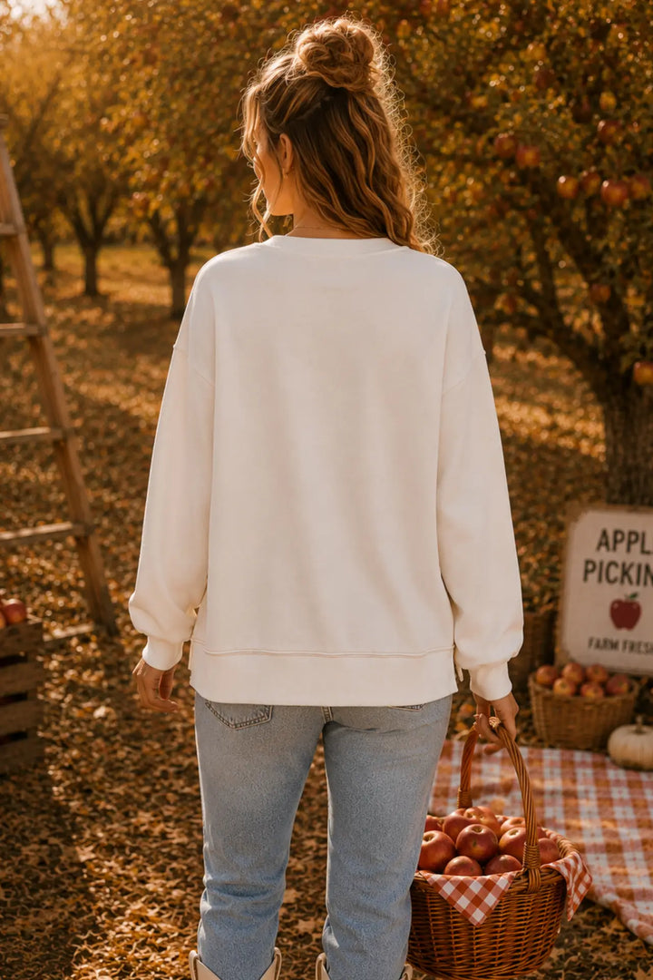 Woman in a white sweater holding a basket of apples in an apple orchard.