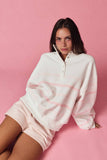 Woman wearing a white oversized sweater with pink stripes on a pink background