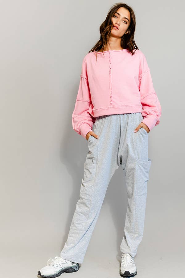 Person wearing a pink sweatshirt and light gray pants on a plain background