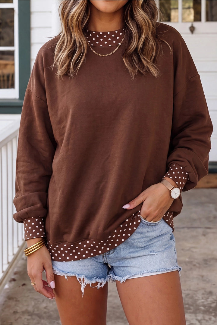 A woman wearing a brown crewneck sweatshirt with white polka dot trim along the collar, cuffs, and hem, paired with light-wash denim shorts.