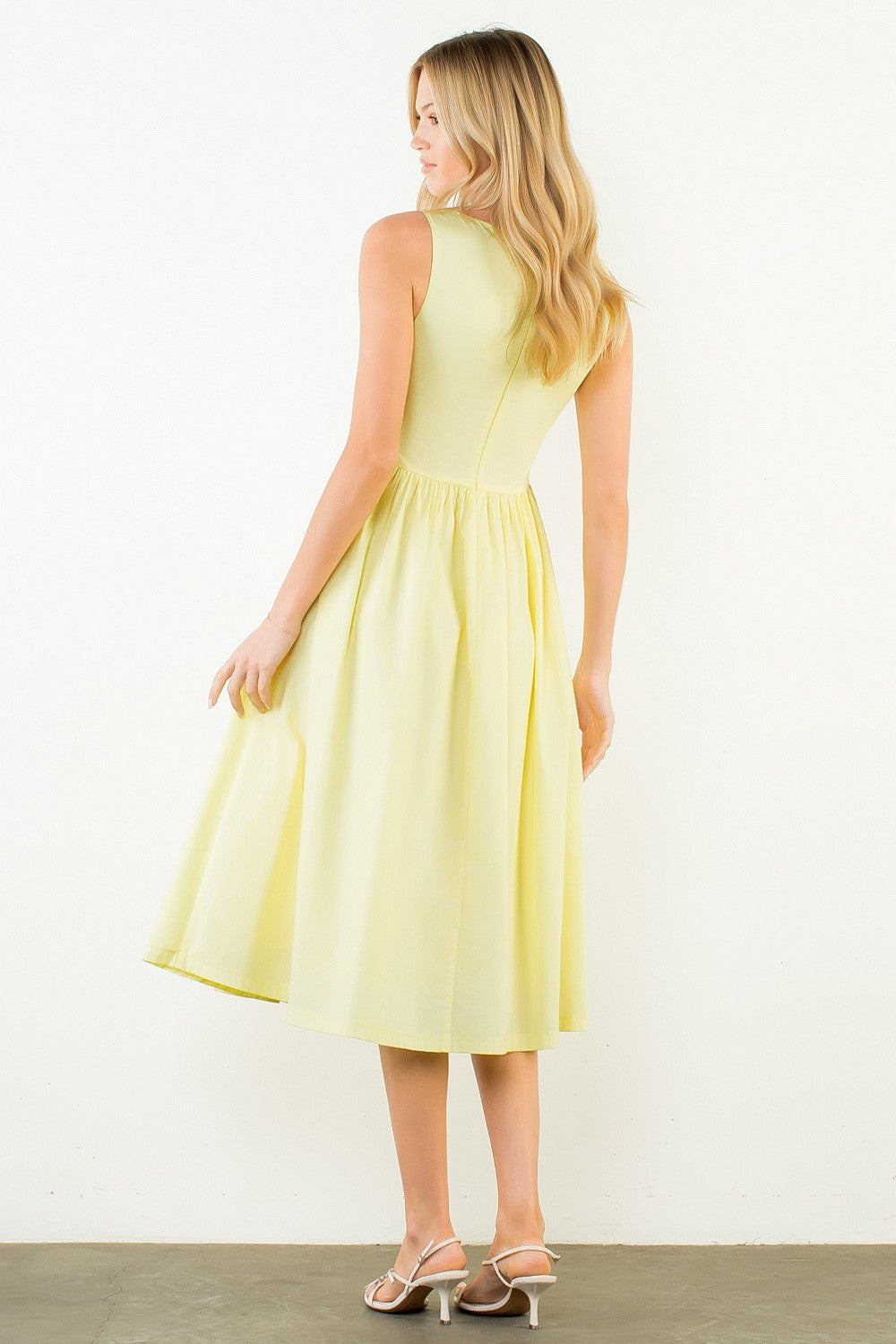 Woman in a light yellow dress standing outdoors with plants around