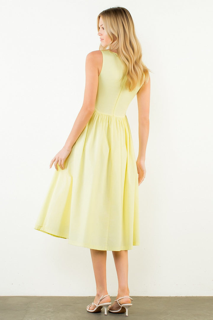 Woman in a light yellow dress standing outdoors with plants around